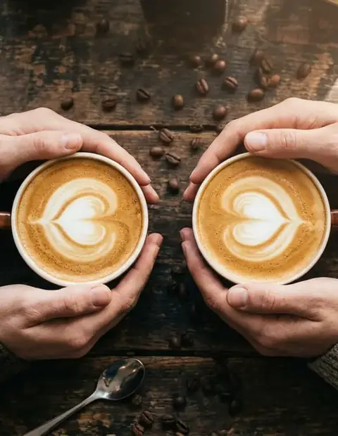 Two latte cups held over a dark table, seen from above